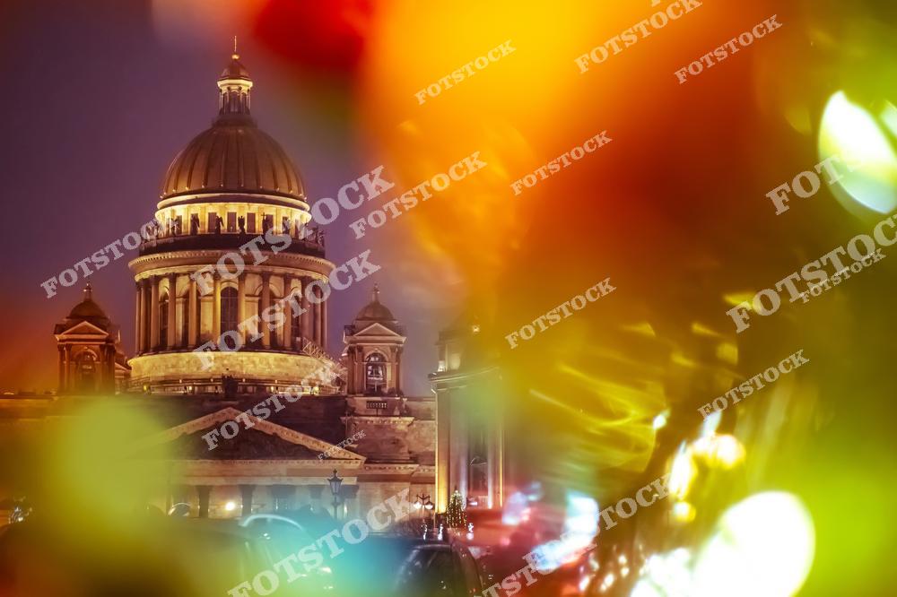 На снимке изображен Исаакиевский собор в Санкт-Петербурге, подсвеченный в вечернее время. Яркие размытые огни на переднем плане создают эффект праздничного сияния. Этот снимок сочетает в себе красоту архитектуры и праздничное настроение города, подчеркивая уникальную атмосферу зимнего Петербурга.